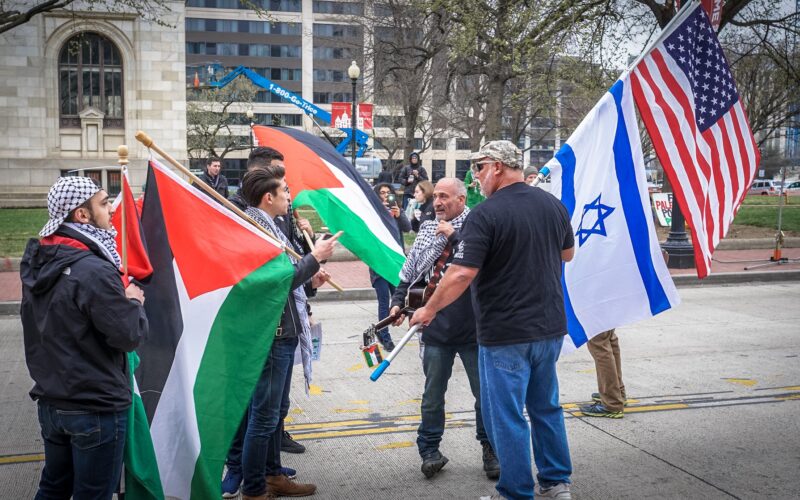Pessoas lutando em prol da causa Palestina, usando a bandeira palestina e sionistas defendendo o Estado de Israel, usando a bandeira de Israel e dos Estados Unidos