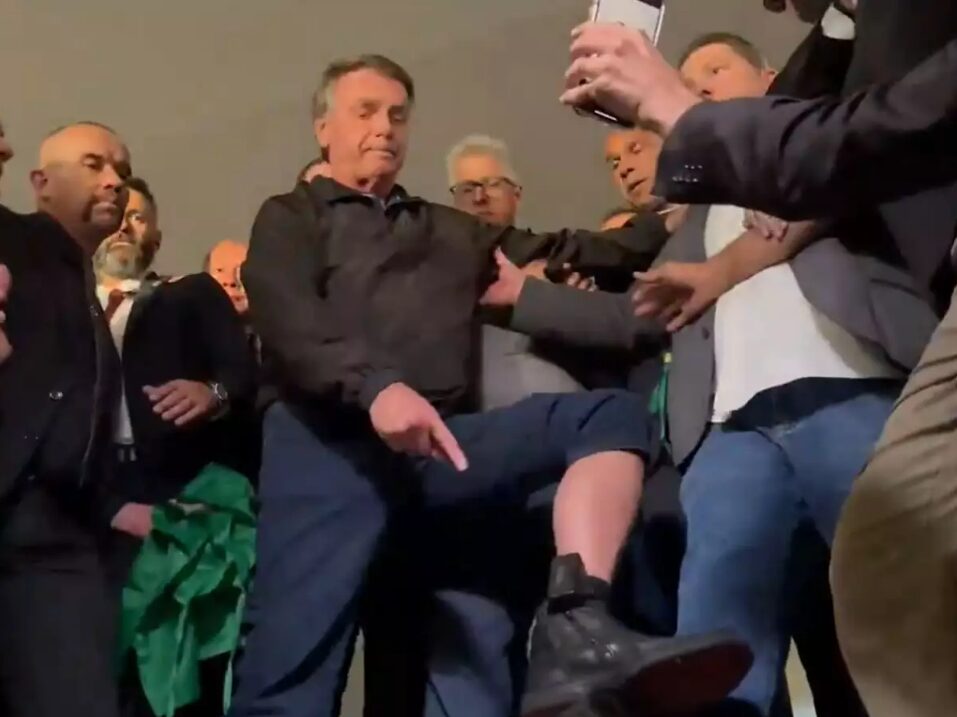 Jair Bolsonaro cercado por apoiadores apontando para a sua tornozeleira eletrônica