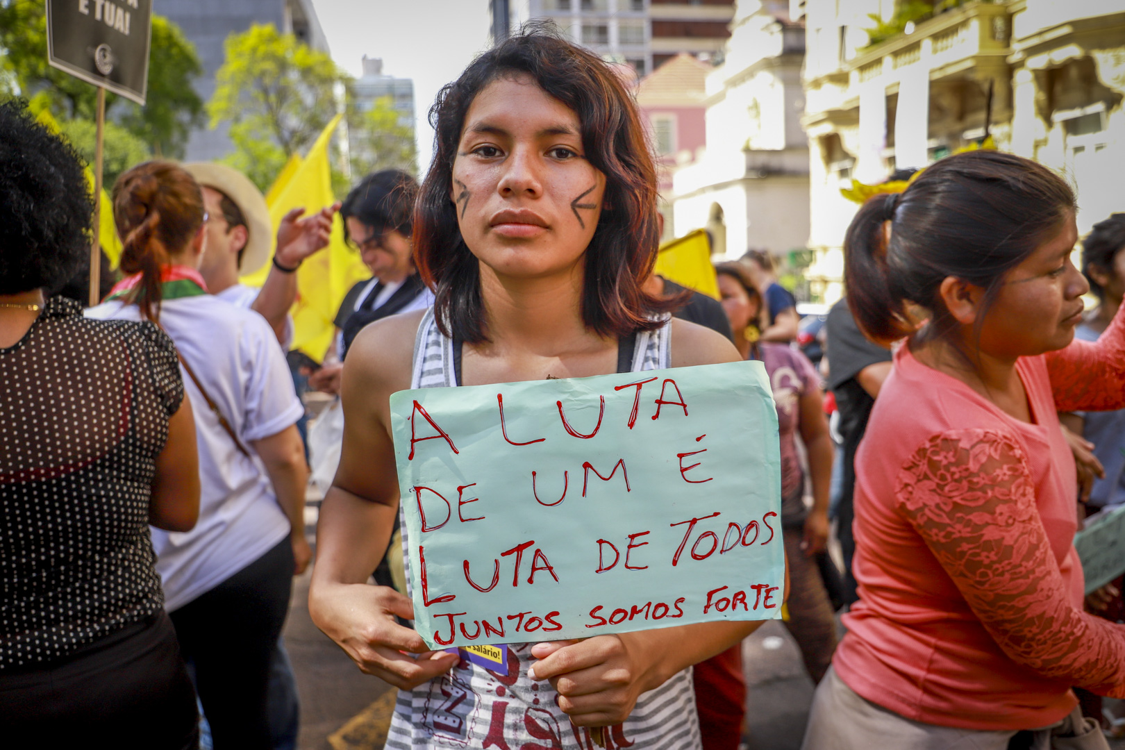 Mulher, supostamente, parda segurando um cartaz em que está escrito "A luta de um é luta de todos. Juntos somos fortes".