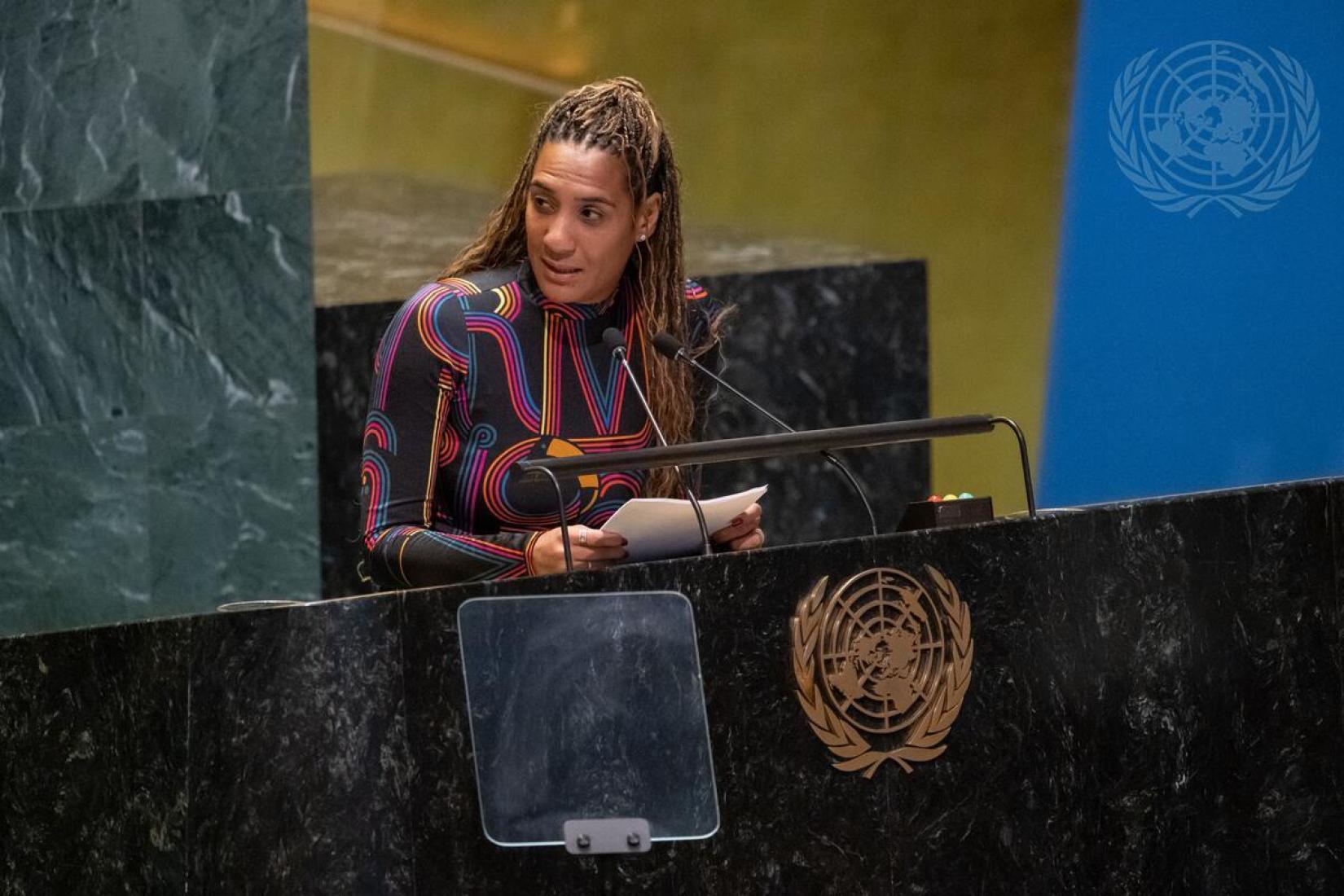 Anielle Franco discura na ONU. Ela segura um papel e olho para o lado. No pleito em que ela está, tem o símbolo da ONU.
