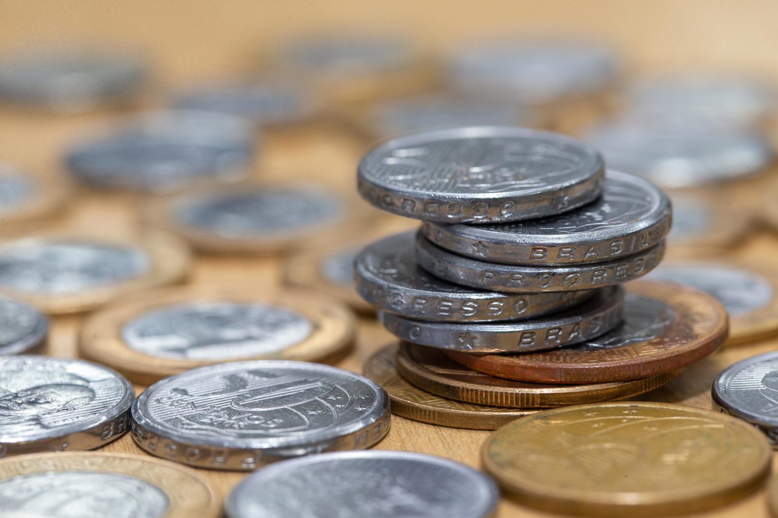 Imagem de moedas de 50 centavos e 1 real, o que remete ao termo "orçamento". Elas estão empilhadas.