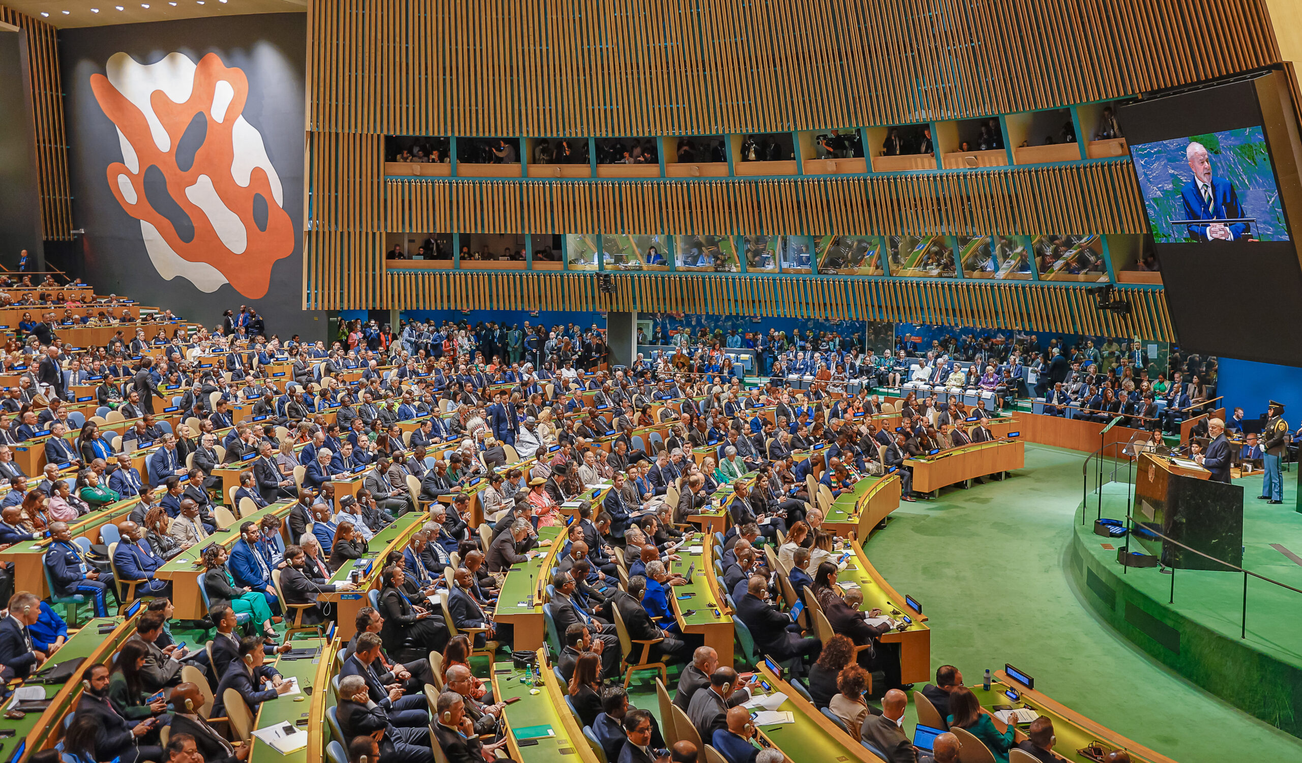 Símbolo da diplomacia tradicional, a imagem é uma foto da Assembleia Geral da ONU. O presidente Lula discursa na frente.