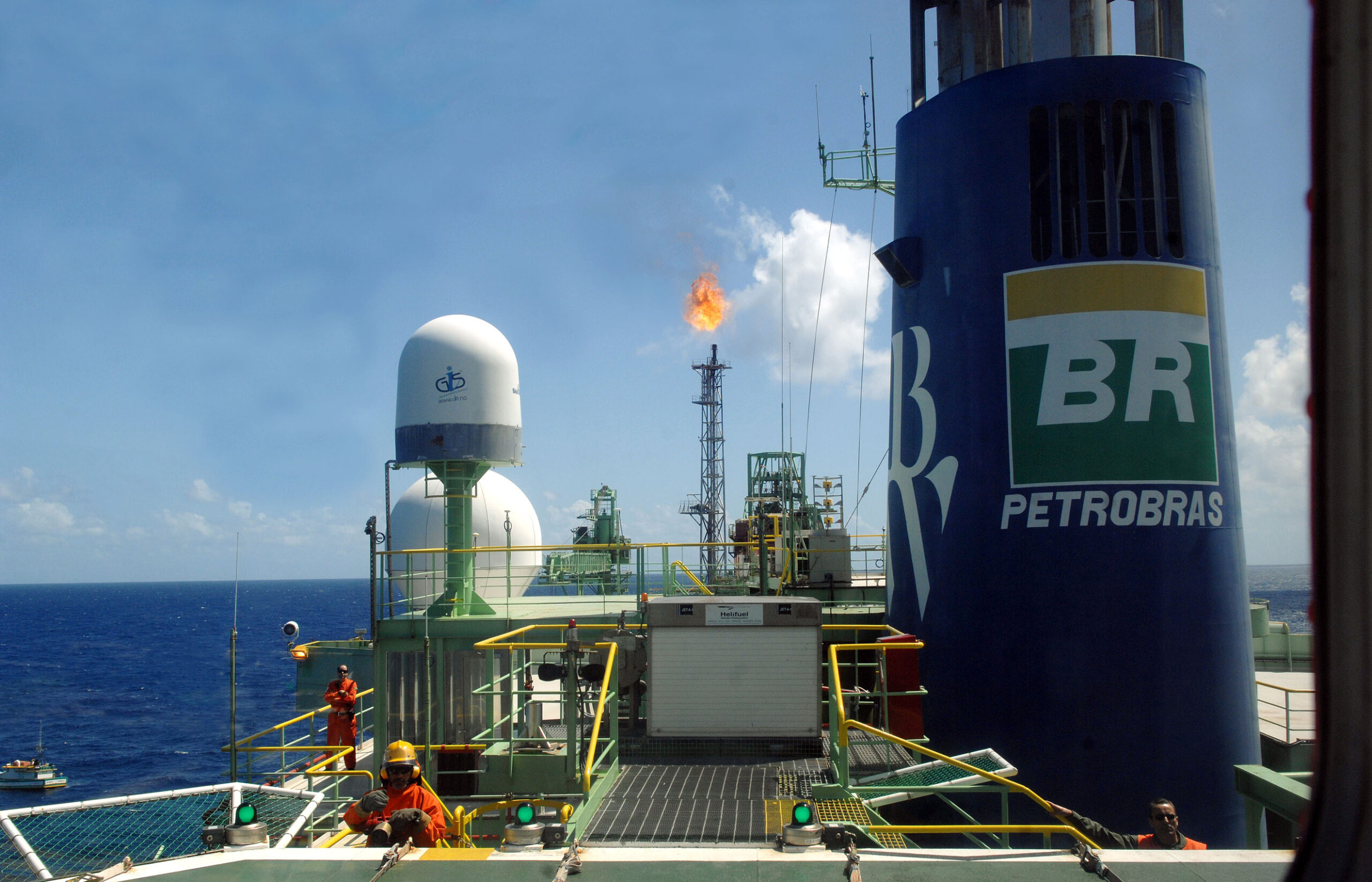 Foto de uma plataforma da Petrobras. Existem dois trabalhadores vestindo laranja