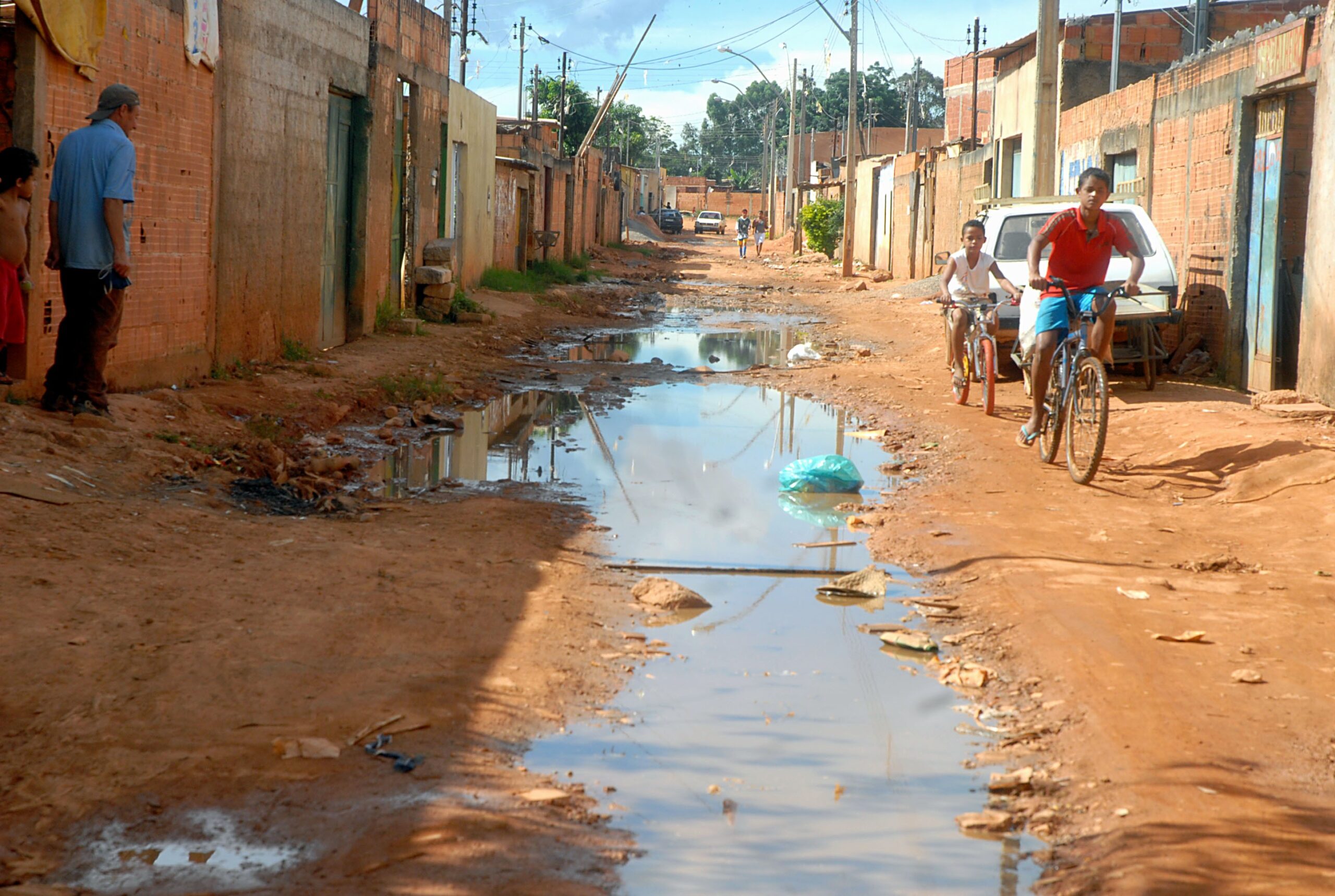 Saneamento básico: pessoas transitando em uma rua com esgoto aberto e de terra.