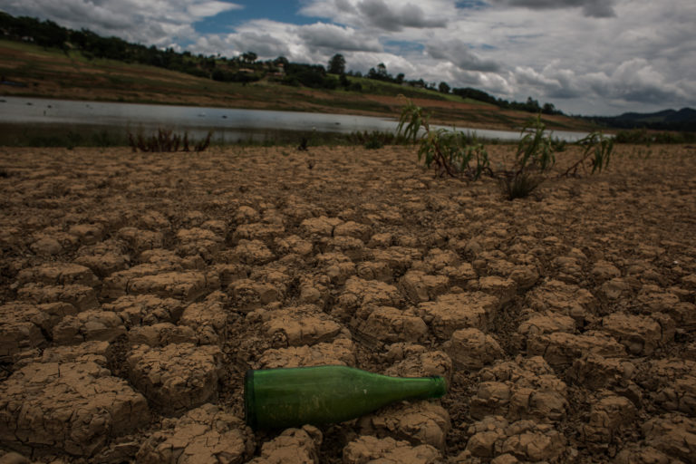 Fotografia de uma represa seca, aparentando apenas um pequeno córrego de água, ao fundo