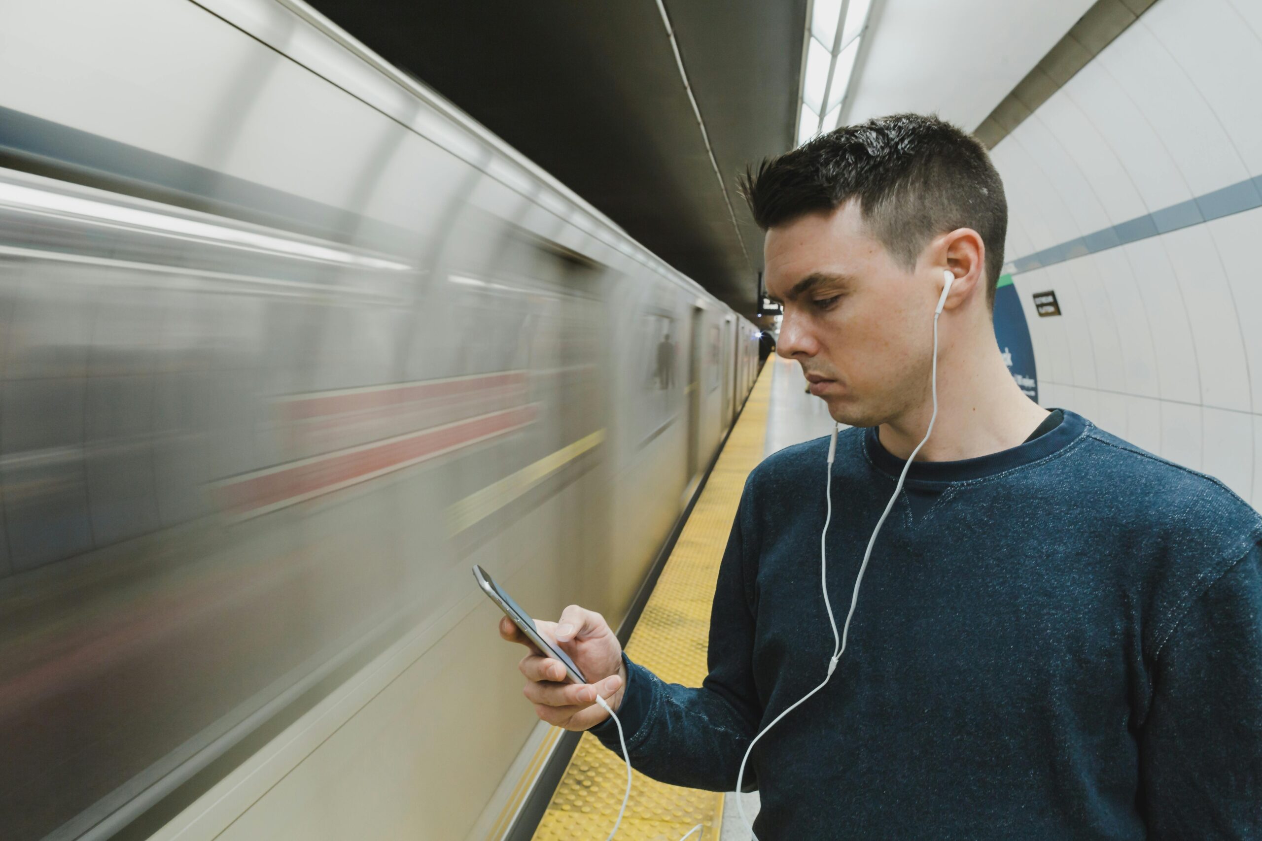 Fotografia de um homem jovem ouvindo música em um fone de ouvido na frente do metrô