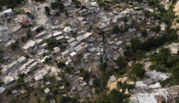 Fotografia de uma região haitiana após o terremoto de 2010. As casas e árvores estão derrubadas