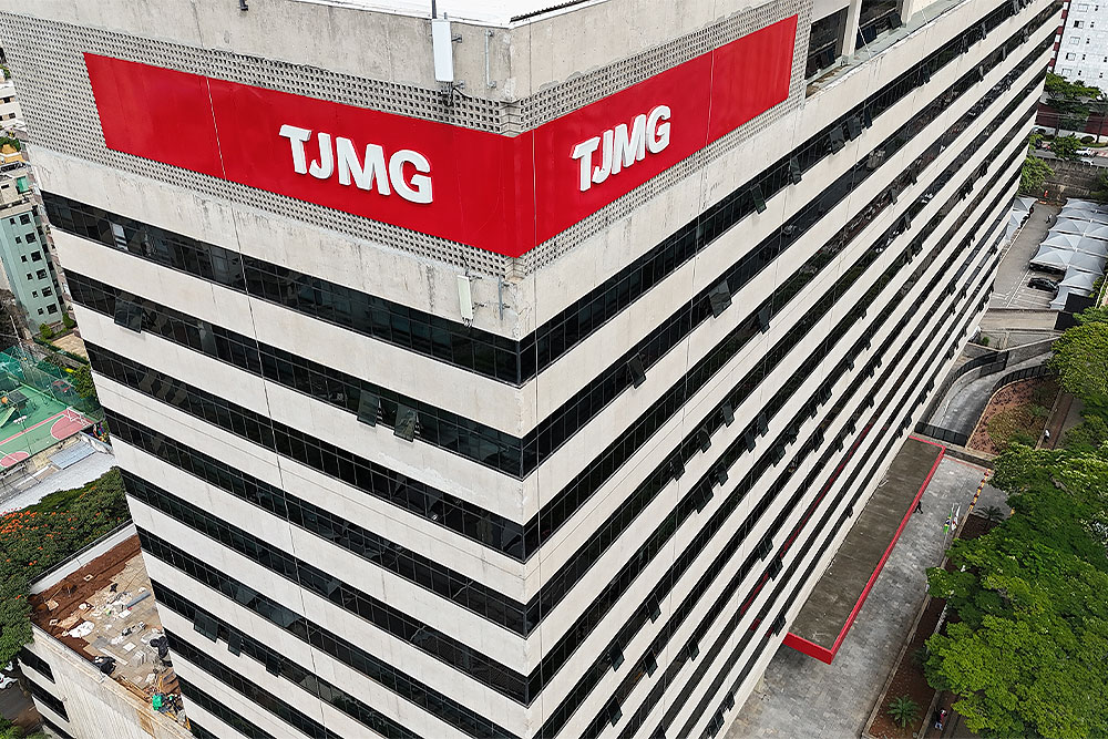 Foto do prédio do TJMG. é um prédio de cor bege, com uma fachada vermelha escrito "TJMG"